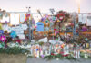 Memorial with candles, flowers, and signs against metal fence.