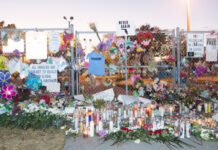 Memorial with candles, flowers, and signs against metal fence.