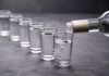 Vodka being poured into a line of shot glasses.