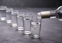 Vodka being poured into a line of shot glasses.