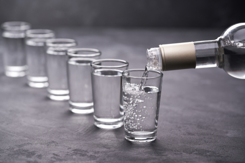 Vodka being poured into a line of shot glasses.