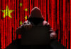 Hooded figure using laptop, China flag background with code.