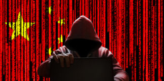 Hooded figure using laptop, China flag background with code.