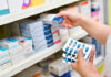 Person selecting medication from pharmacy shelf.