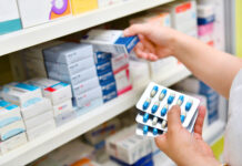 Person selecting medication from pharmacy shelf.