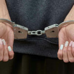 Handcuffed person with painted nails in dark clothing.