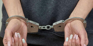 Handcuffed person with painted nails in dark clothing.