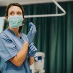 Hospital Executives ARRESTED — Shielded Killer Nurse… Nurse wearing scrubs and mask putting on gloves.