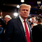 Trump Hijacks Iconic Legend—Daughter Fires Back Hard… A serious-looking man in a suit with a red tie surrounded by a crowd and cameras
