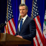 Governor Gavin Newsom speaks at podium with flags behind.