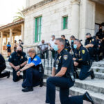 Mayor’s Shocking Fraud Scheme Exposed! Police officers kneeling on steps, some wearing face masks.