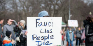 Person holding sign that reads Fauci Lies People Die
