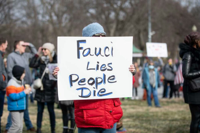 shutterstock_2115278627-1.jpg Person holding sign that reads Fauci Lies People Die