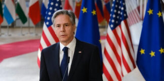 Man in suit speaking at podium with international flags behind