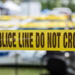 Mystery Corpse Rattles Queens Yellow police tape that says, Police Line Do Not Cross.