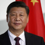 Xi Strengthens China–North Korea Ties Man in suit standing before Chinese flag.
