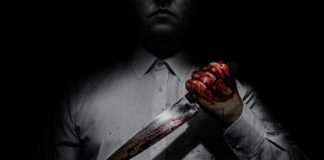 Person holding bloody knife in dark lighting.