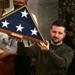 Brussels Signals Long-Term Ukraine War Support Strategy Man holding folded American flag in wooden case.