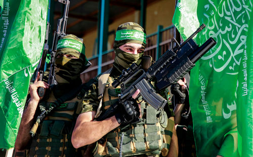 shutterstock_1979836574 Two armed masked soldiers with green flags.
