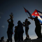 Cuba’s Fake Opening: Power Grab Exposed Silhouetted crowd waving Cuban flags at dusk