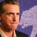 Newsom Redrew Kiley’s District—He’s Still Standing A serious-looking political figure at a press event with a bear graphic in the background