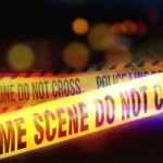 Hate Crime Fears – Grandfather Shot in Daylight Yellow police tape marking a crime scene with blurred lights in the background