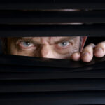 Drone Maker Stalked—Kremlin Link Alleged Man peeking through half-open black blinds.