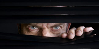 Man peeking through half-open black blinds.