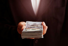 Budget Crunch, DEI Paychecks Soar Hand holding a stack of US dollars.