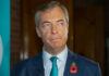 man in suit with teal tie and red poppy pin looking to the side