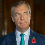 man in suit with teal tie and red poppy pin looking to the side