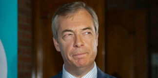 man in suit with teal tie and red poppy pin looking to the side