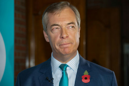 man in suit with teal tie and red poppy pin looking to the side