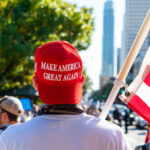 Media Spin Targets Massive Patriotic Blowout Person wearing a red Make America Great Again hat holding an American flag at a rally