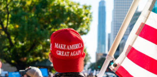 Person wearing a red Make America Great Again hat holding an American flag at a rally