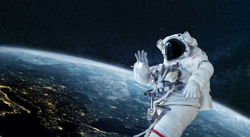 shutterstock_1936566580 Astronaut floating in space above Earth, waving.