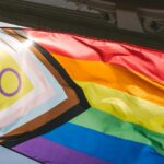 Hands holding a colorful pride flag against a bright sky
