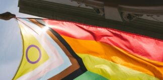 Hands holding a colorful pride flag against a bright sky