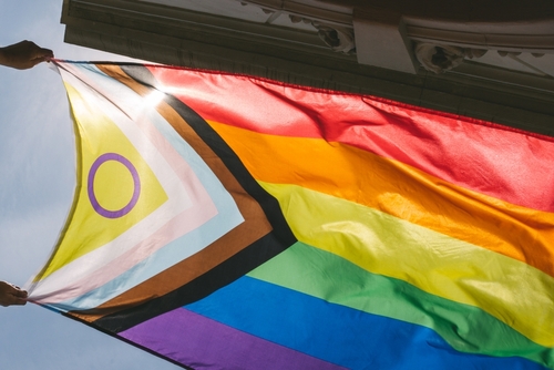 Hands holding a colorful pride flag against a bright sky