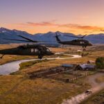 Black Hawks Storm Flooded Kids’ Camp Two military helicopters flying over a rural landscape at sunset