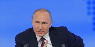 A political leader speaking at a press conference with a serious expression