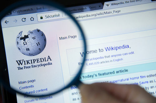 Wikipedia homepage viewed through a magnifying glass.